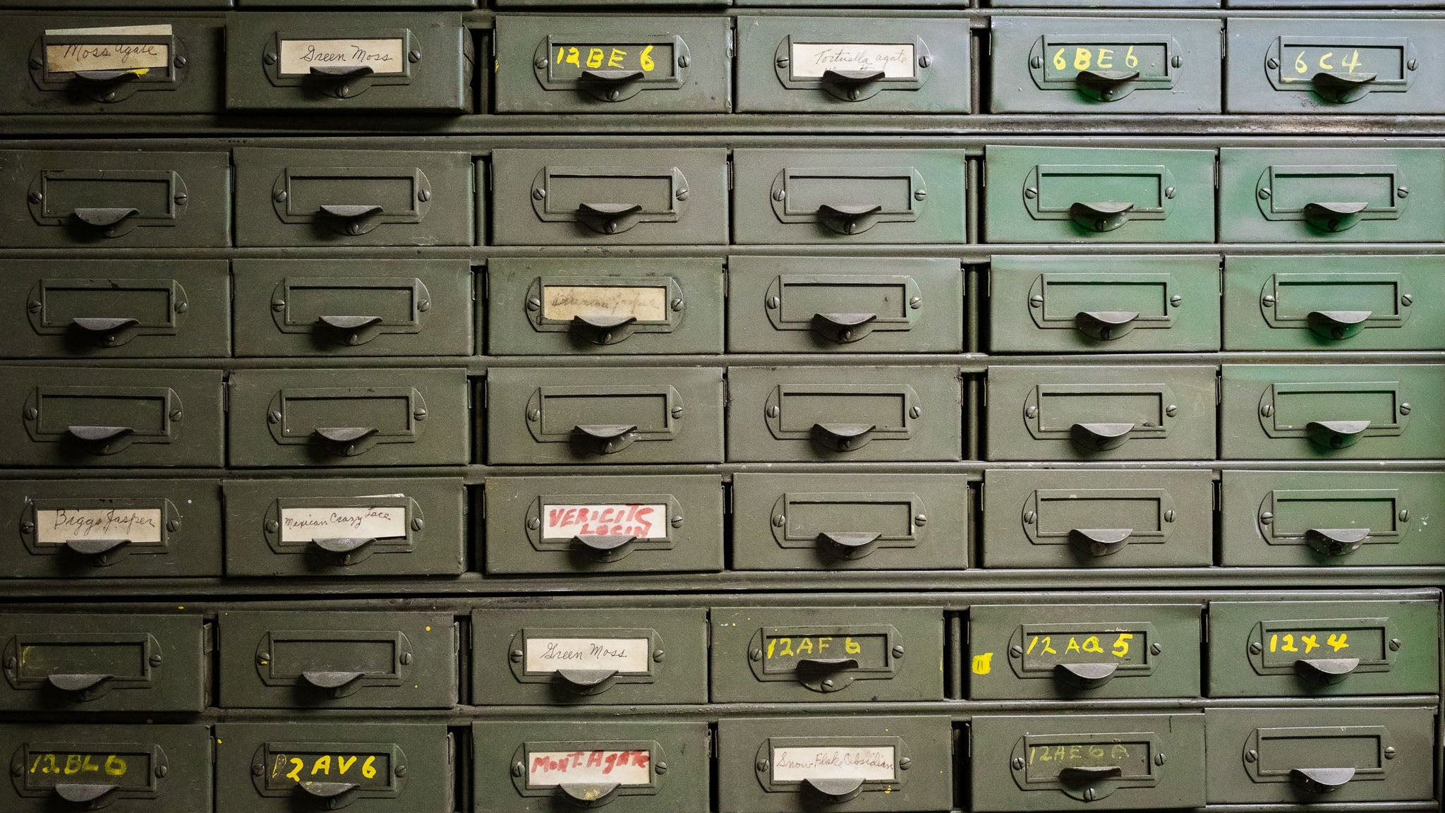 Row of green metal drawers with labels of gems and minerals